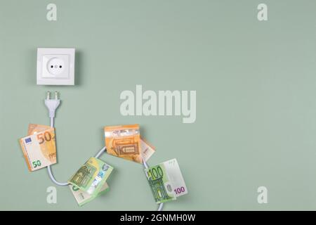 Electric power plug with euro banknotes on it and electric socket on light green background. Electricity cost and expensive energy concept Stock Photo