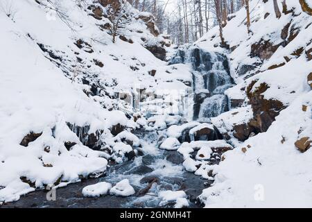 Small waterfall of cold water flow among the stones covered with snow Stock Photo