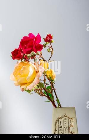 Photograph of a bouquet of natural flowers of red and yellow roses in a handmade vase on a light blue background.The photo has copy space to put text Stock Photo