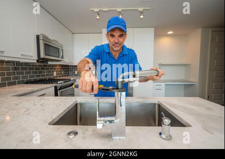Plumber in blue uniform using pliers to repair or install a kitchen faucet Stock Photo