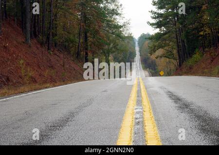 Deserted straight highway through fall trees in rain Stock Photo