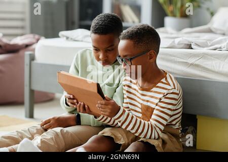 Portrait of two boys using tablet together while sitting on floor at home and watching videos Stock Photo