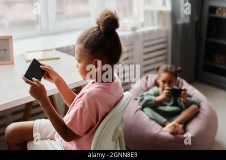 Portrait of two cute girls using smartphones and playing mobile games at home, copy space Stock Photo