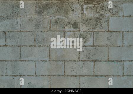 Full frame background of gritty concrete brick wall has a weathered surface of faded paint that is peeling off. Stock Photo
