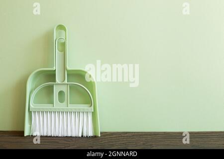 Green broom and dustpan on wooden table. green wall background. Cleaning housework concept Stock Photo