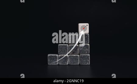 Risingup arrow from below to the top on chart steps with black and white dice blocks with target icon on dark background, minimal style. The business Stock Photo