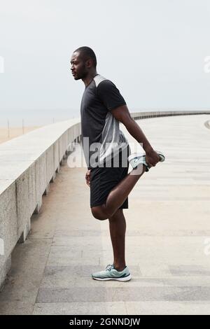 African sportive man doing stretching exercises during morning training outdoors Stock Photo