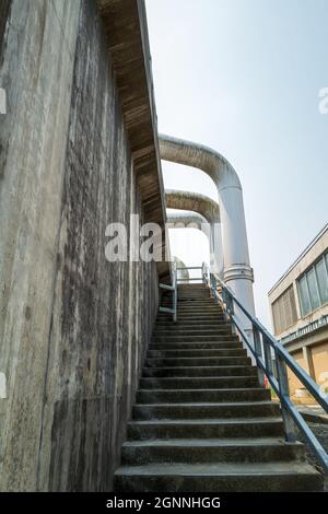 Large pipes reaching over the exterior stairway of a concrete building Stock Photo