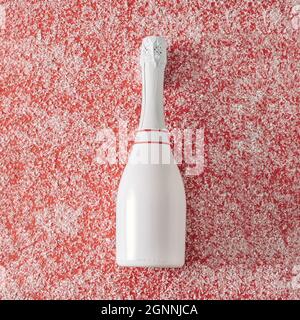 Christmas background with pure white unlabelled champagne bottle over a red background with scattered winter snow viewed side on with copy space for a Stock Photo