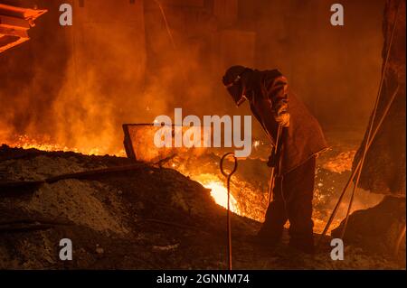 The process of releasing pig iron from a blast furnace. A man works with molten metal Stock Photo