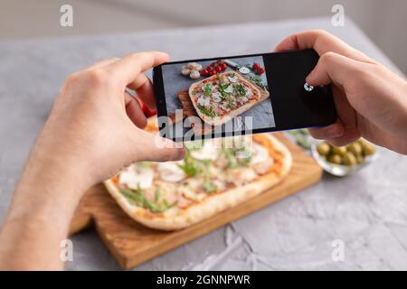 Chef takes pictures of the cooked of italian pizza with parma ham on smartphone. Photographing food and social networks concept Stock Photo