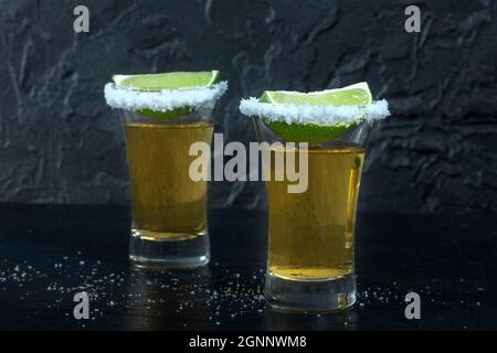 Tequila shots, with salt rims and lime slices, on a dark background, side view Stock Photo