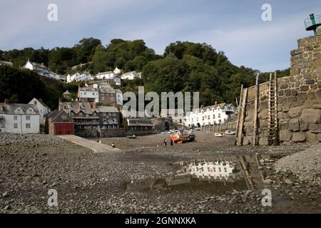 Clovelly harbour at low tide with moored fishing boats and mooring poles on harbour wall amd Red Lion Hotel reflected in rock pool North Devon Stock Photo