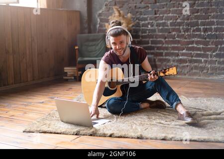 Caucasian young adult learning guitar online music class with distant teacher computer mobile device. Handsome hipster man teaching music through lapt Stock Photo