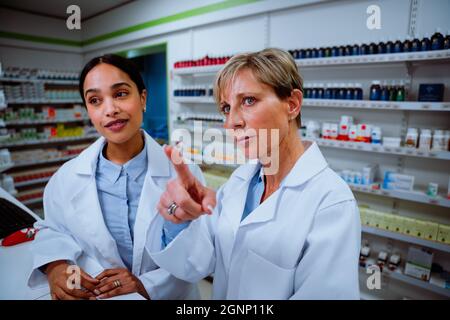 Senior female pharmacist training new student assistant pointing and naming medication in pharmacy working on digital tablet  Stock Photo
