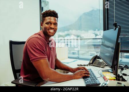 Mixed race male designer smiling while researching through layout designs on desktop computer Stock Photo