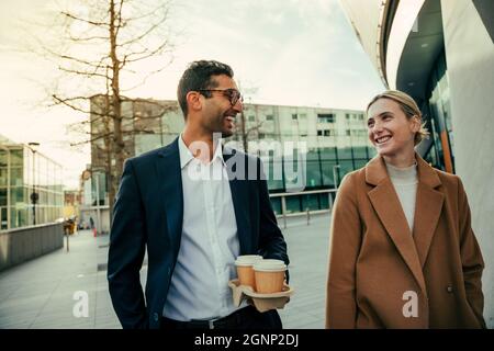 Smiling mixed race colleagues bonding while walking to work enjoying hot coffee and brainstorming ideas  Stock Photo