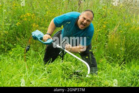 man with a lawn mower. electric trimmer. gardener mows the grass with an electric scythe. Stock Photo