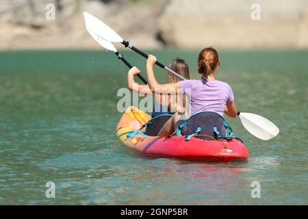 Back view portrait of two women rowing in a tandem kayak in a lake Stock Photo