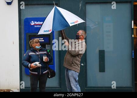 Ashford, Kent, UK. 27 Sep, 2021. UK Weather: A band of heavy rain sweeps across the country with windy weather seen here in the town centre of Ashford as local shoppers hurry through the high street as a deluge of rain falls. A man quickly puts up his umbrella before he gets soaked. Photo Credit: Paul Lawrenson /Ģ����ý Live News Stock Photo