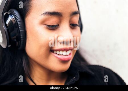 portrait of a cheerful young asian woman with headphones enjoying listening to music outdoors Stock Photo
