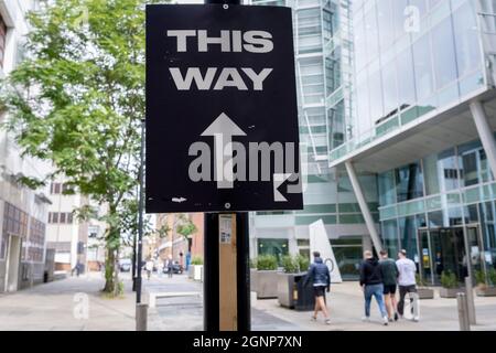 Pedestrians walk in the direction of a sign pointing straight ahead, a direction for something unknown happening this way, in a City of London sidestreet, on 22nd September 2021, in London, England. Stock Photo