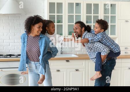 Happy African American parents piggy backing little kids in kitchen Stock Photo
