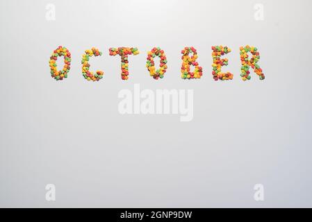 October inscription on a white background. Confectionery sprinkles in the form of multi-colored maple leaves Stock Photo