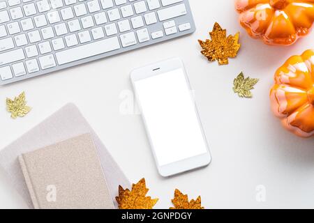 Autumn desk table with computer keyboard, smartphone mockup, pumpkins, paper notebooks and maple leaves. Flat lay, top view. Stock Photo