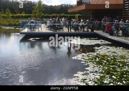 People in the Outdoor Seating Area of the Café by the Lake in the Welcome Building at RHS Garden Bridgewater, Worsley, Manchester, UK. Stock Photo