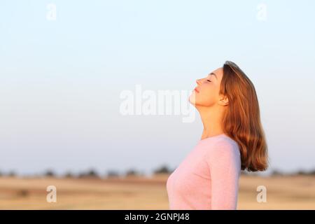 Side view portrait of a relaxed woman breathing fresh air at sunrise in a field Stock Photo