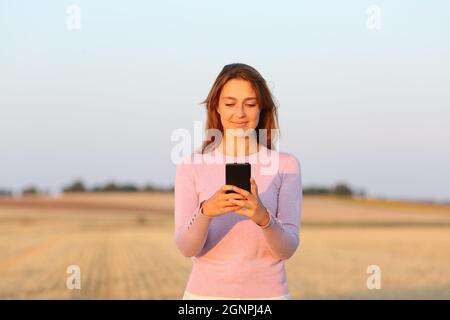 Front view of a happy woman using smart phone in harvested field Stock Photo