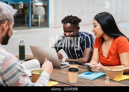 Diverse people eating takeaway food while using laptop computers outdoor - Focus on asian girl face Stock Photo