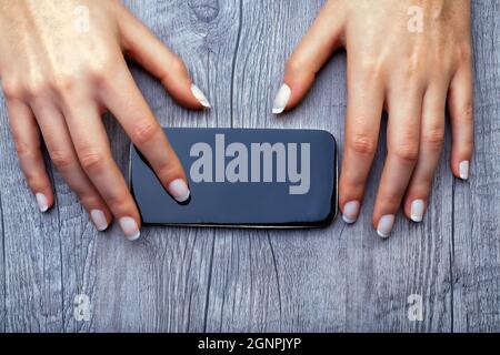 view from above: hands with smartphone on table, the touchscreen has ample copyspace available for compositing  (horizontal version) Stock Photo