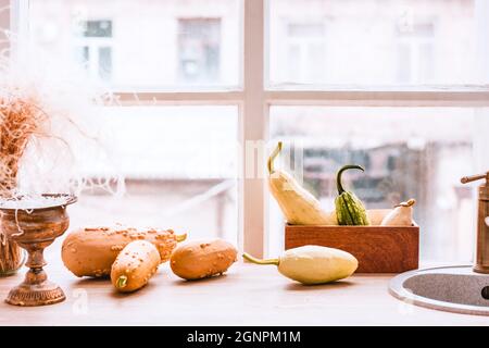 Orange and yellow autumn pumpkins, sink and tableware on a kitchen table in front of a window. Comfortable, interior home design for fall season Stock Photo