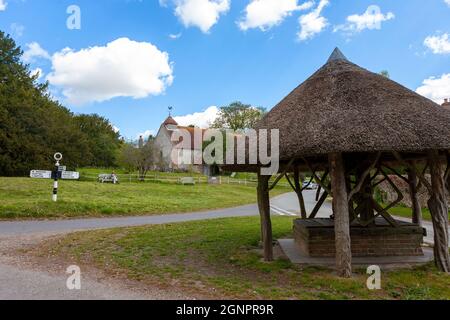 Thatched well on the village green and St. Peter's church beyond, East Marden, West Sussex, UK Stock Photo