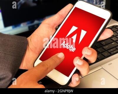 California, United States-2021. Adobe Mobile Application Opened on smartphone screen with man holding in front of laptop. Editorial adobe concept back Stock Photo