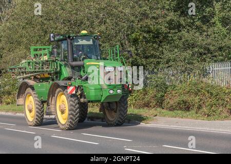 Familiar green John Deere farm self-propelled sprayer unit on open uphill rural country road. Deere model is R 4140i. Stock Photo