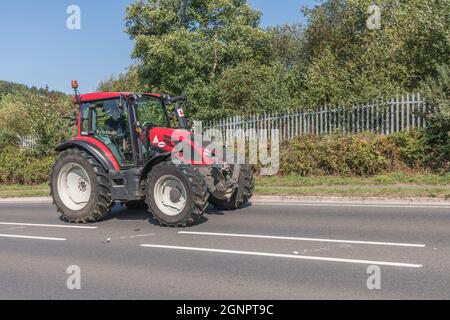 Front 3/4 profile of red Valtra farm tractor on open uphill rural country road. Valtra is a Finnish tractor brand, this is G Series G136 model. Stock Photo