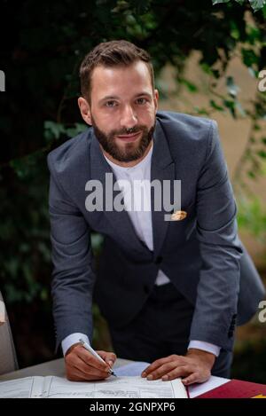 A vertical closeup of the man in a dark gray suit signing a document and smiling. Stock Photo