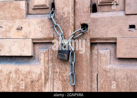 Rusty black padlock on a chain on an old vintage wooden closed door. Close-up. Entrance is a forbidden concept Stock Photo