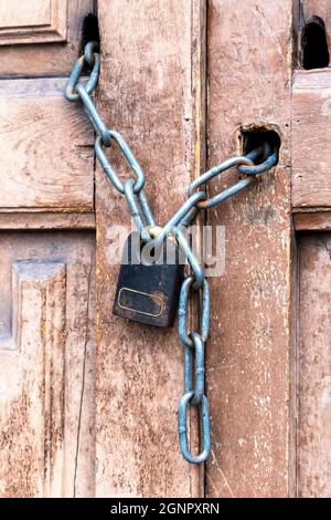 Rusty black padlock on a chain on an old vintage wooden closed door. Close up. Entrance is a forbidden concept. Vertical view Stock Photo