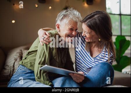 Portrait of happy senior mother with adult daughter indoors at home, using tablet. Stock Photo
