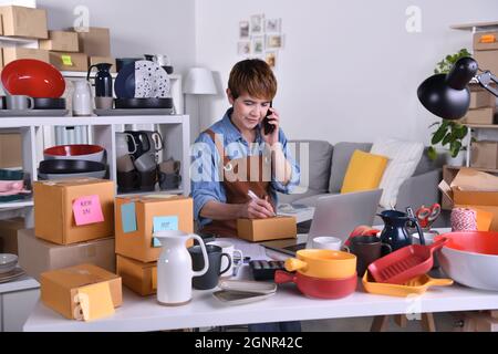 Mature Asian woman entrepreneur, Business owner working at home office confirming orders from customer on the phone. Online web store owner taking ord Stock Photo