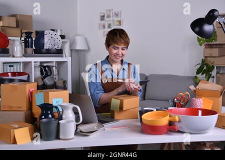 Mature Asian woman entrepreneur, Business owner working on digital tablet checking address and delivery detail before shipping product. Online selling Stock Photo