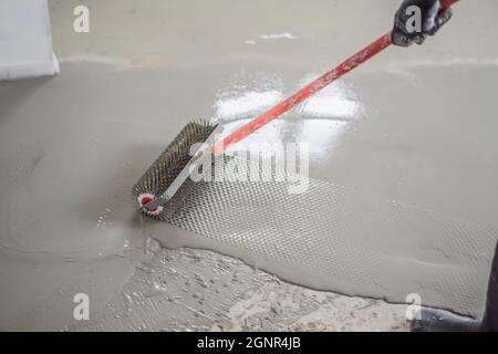 plasterer during floor covering works with self-levelling cement mortar, uses a needle roller Stock Photo