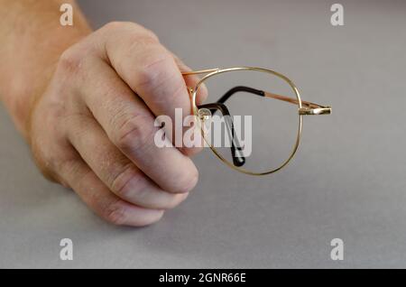 One hand holds an empty metal eyeglass frame against a gray back Stock Photo