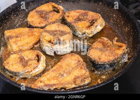 Sliced fresh bonito fish fried in frying pan on black stove. Selective focus Stock Photo