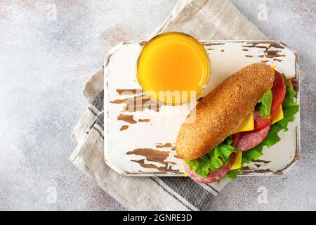 Healthy sandwiches with bran bread, green lettuce, cheese, red tomato and sliced salami on parchment paper and rustic wooden stand. Breakfast concept. Stock Photo