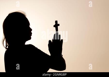 Silhouette of faithful woman praying with chrisrtian cross at sunset ...